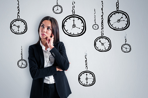 Attractive young european businesswoman with folded arms standing on concrete wall background with creative hand drawn clock sketch. Time management, deadline and career concept