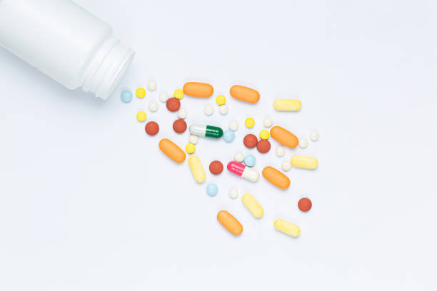 istock Flat lay composition with bunch of different colorful pills scattered on table from popped plastic bottle. Pile of opened medication on white paper textured background. Close up, copy space for text 1332529453