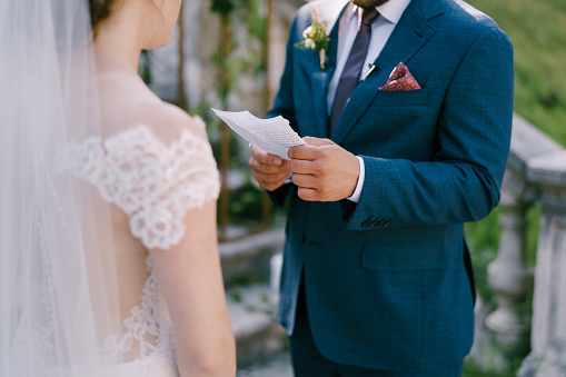 Groom reads an oath from a sheet of paper to bride in a white dress. Close-up. High quality photo