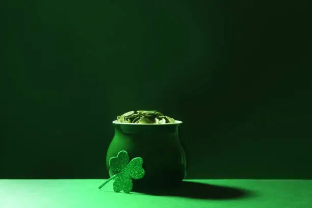 Photo of Pot of gold coins and clover on green table against dark background. St. Patrick's Day celebration