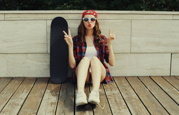 Happy smiling young woman sitting with skateboard wearing a baseball cap on city street Happy smiling young woman sitting with skateboard wearing a baseball cap on city street woman wearing baseball cap stock pictures, royalty-free photos & images