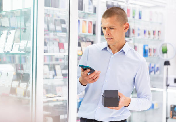 istock Smiling male holding mobile phone in the hand at electronics store 1332535730