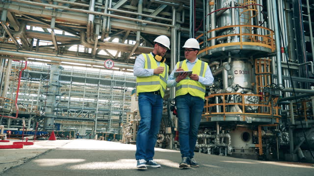 Male colleagues are walking along the premises of the refinery plant