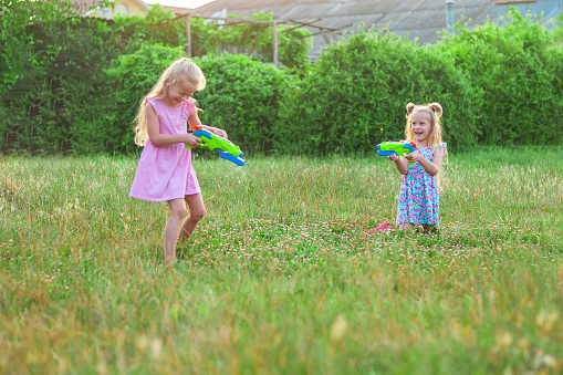 two little girls play in the summer on a green meadow with water pistols. High quality photo