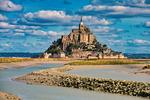 Mont Saint-Michel on tidal Island under sunny summer skyscape. Aerial Drone Point of view from the Atlantic Ocean Side over Mont Saint Michel towards the Normandy Coast. Mont Saint-Michel, Avranches, Manche, Normandy, France, Europe