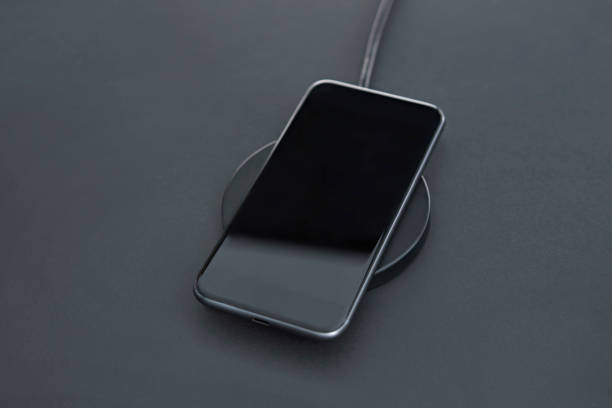 istock Close-up of luxury smartphone while recharging battery using wireless charger. Matt grey desk surface in background. 1332547708