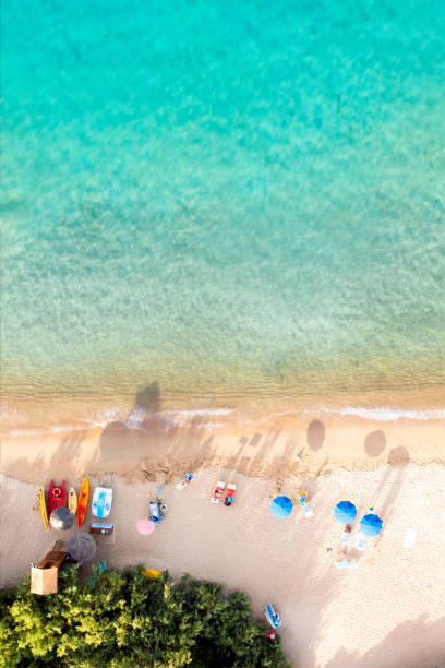 View from above, stunning aerial view of a white sand beach bathed by a turquoise water and relaxed people under some beach umbrellas at sunset. Cala di volpe beach, Costa Smeralda, Sardinia, Italy. View from above, stunning aerial view of a white sand beach bathed by a turquoise water and relaxed people under some beach umbrellas at sunset. Cala di volpe beach, Costa Smeralda, Sardinia, Italy. Cala Di Volpe stock pictures, royalty-free photos & images