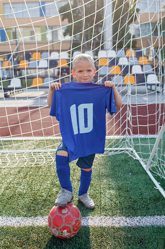 Young soccer player holding a blue jersey with ten number before training on open field in the yard. Little football fan with sportswear, number of legend and superstar