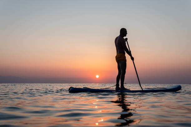 istock Silhouette of man paddleboarding at sunset 1332555388
