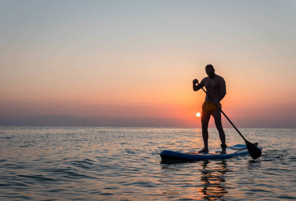 istock Silhouette of man paddleboarding at sunset 1332555478