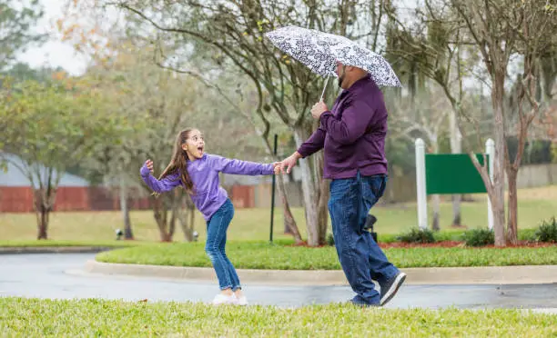 Photo of Hispanic girl pulling father's hand, playing in the rain