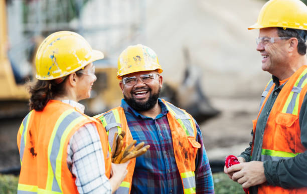 Three multi-ethnic construction workers chatting A group of three multi-ethnic workers at a construction site wearing hard hats, safety glasses and reflective clothing, smiling and conversing. The main focus is on the mixed race African-American and Pacific Islander man in the middle. The other two construction workers, including the woman, are Hispanic. resting photos stock pictures, royalty-free photos & images