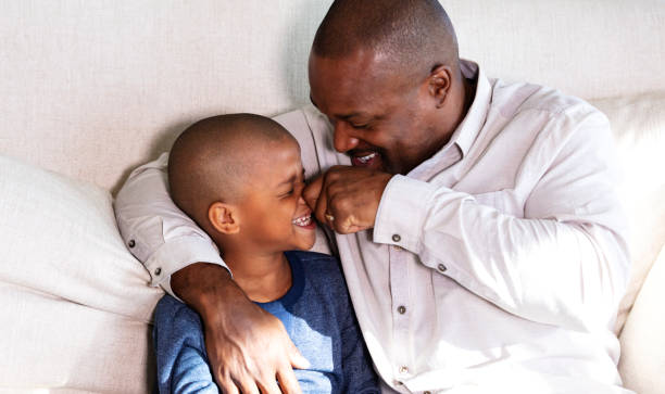 African-American father on couch, making son laugh