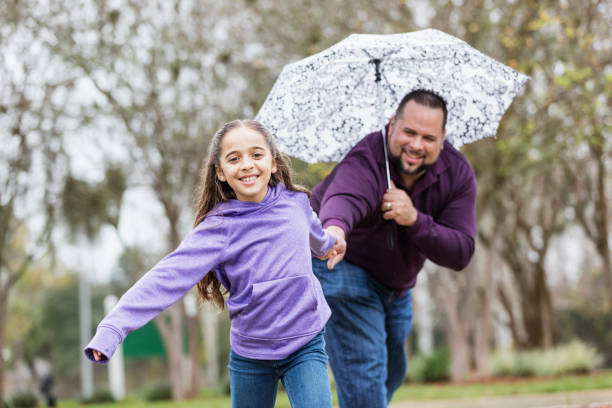 istock Hispanic girl pulling father's hand, playing in the rain 1332568701