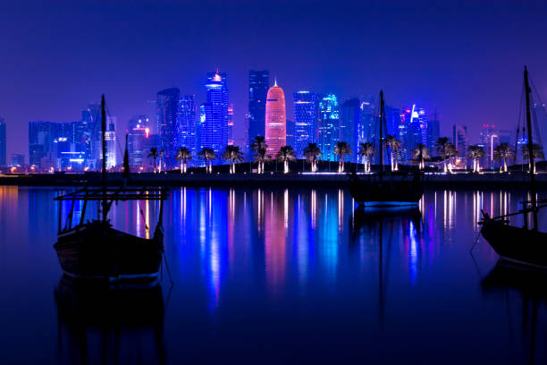 skyline illuminato coloful di doha di notte con le tradizionali barche di legno chiamate dhows in primo piano, qatar - middle eastern architecture foto e immagini stock