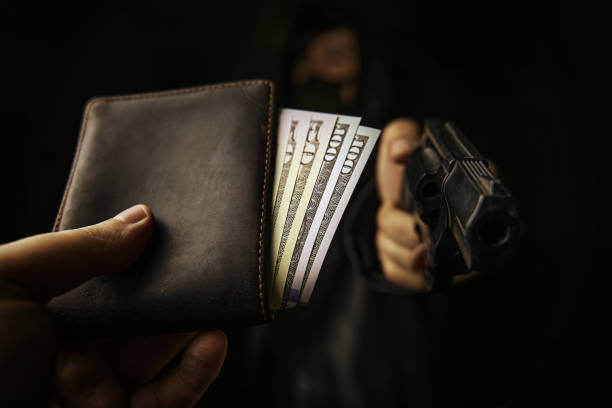 Assault on unarmed man. Armed robbery. Assault on unarmed man. Man's hand holds out wallet of money to robber with gun. Hundred and fifty dollars in open purse.Firearm is pointed at camera. wallet gun stock pictures, royalty-free photos & images