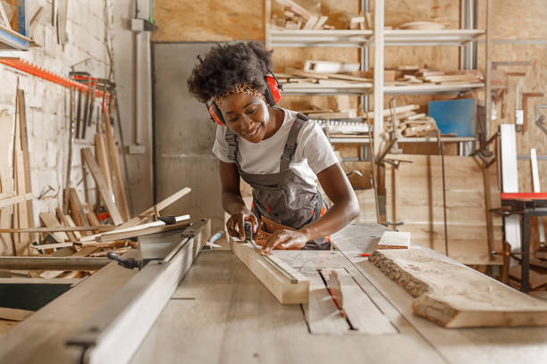 istock A Female Carpentry Worker of African-American Ethnicity is Working in Large Workshop Using a Measuring Tape to Mark the Wooden Plank. 1332575875