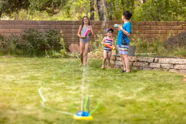 High quality stock photos of family kids playing in the sprinkler and having a squirtgun fight.
