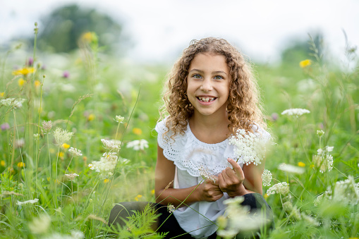 Adorable little girl in blooming dandelion meadow on beautiful spring day. Child having fun outdoors picking fresh flowers.