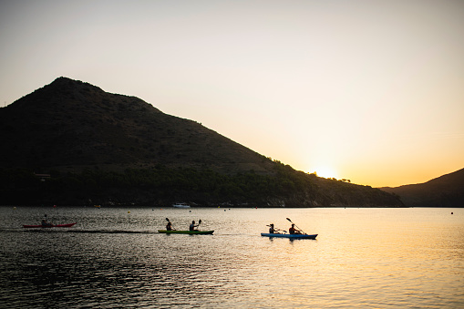 Male and female friends paddling single and tandem kayaks in Mediterranean Sea off the Costa Brava at dawn.