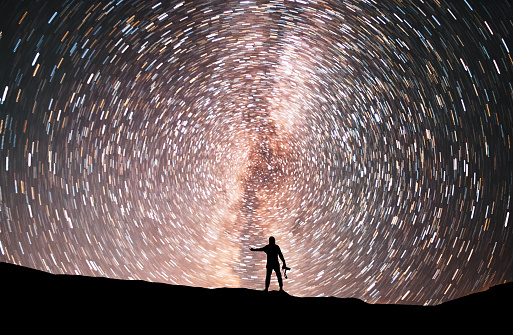 Starry night, silhouette stands on the hill and looking at the colorful star trails on the sky. Night time lapse.