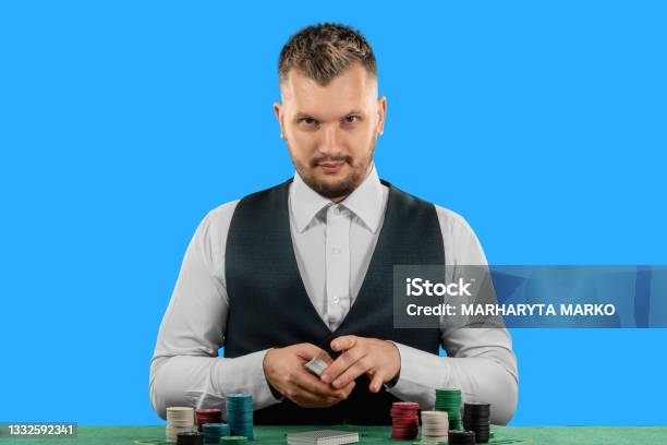 Male Croupier At The Casino At The Table Isolated On Blue Background Casino Concept Gambling Poker Chips On The Green Casino Table Stock Photo - Download Image Now