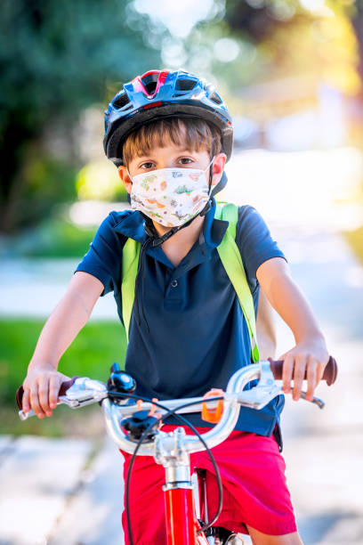 istock Little boy riding his bicycle going back to school carrying his backpack wearing a bicycle helmet 1332601178