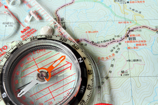 A close up of a woman's hand holding a compass as a road winds its way through Southern California's Peninsular Ranges.