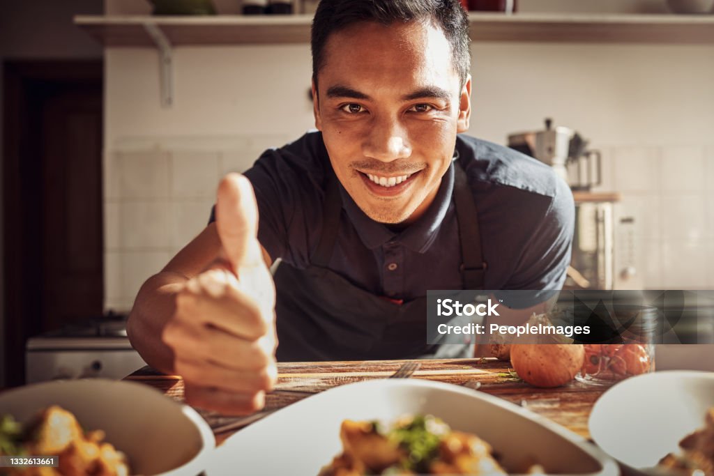 Portrait of a young man showing thumbs up while preparing a delicious meal at home Food fit for a king Chef Stock Photo