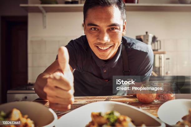 Portrait Of A Young Man Showing Thumbs Up While Preparing A Delicious Meal At Home Stock Photo - Download Image Now