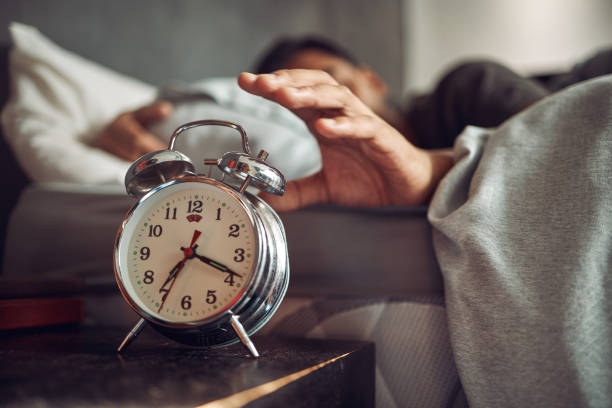 plan d’un jeune homme atteignant son réveil après s’être réveillé dans son lit à la maison - good morning photos et images de collection