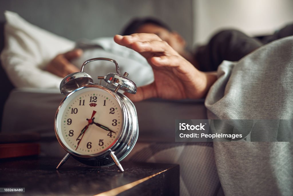 Shot of a young man reaching for his alarm clock after waking up in bed at home Early to bed, early to rise Alarm Clock Stock Photo