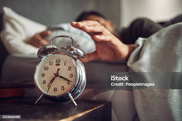 Shot Of A Young Man Reaching For His Alarm Clock After Waking Up In Bed At Home Stock Photo - Download Image Now