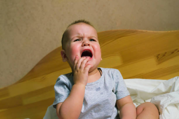 istock baby boy sitting on a white pillow and crying teething. 1332621210