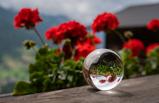 Glass sphere lying on a wooden balcony, red flowers, mountains