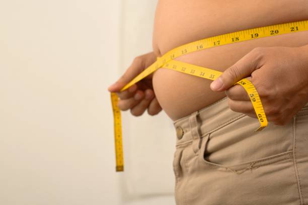 He was measuring his waist with a yellow waist tape because he was too fat. stock photo