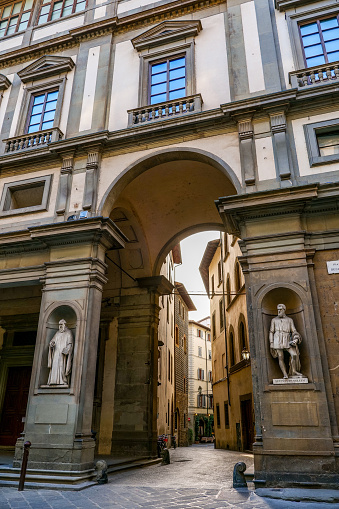 The external facade of the Uffizi Galleries in the historic heart of Florence, with the passage between Piazzale degli Uffizi (Uffizi square) and Lambertesca street. The two statues in the image are part of the 28 statues for the niches of the pillars on the square made between 1842 and 1856, depicting illustrious Tuscan citizens throughout history. Built between 1560 and 1581 by Giorgio Vasari at the behest of the Medici family to house the new offices (Uffizi) of the Florentine government. Currently the Uffizi building is one of the most important international museums. The Uffizi Galleries preserve one of the greatest artistic heritages in the world with works of art by Leonardo da Vinci, Raphael, Sandro Botticelli, Tiziano, Pontormo, Bronzino, Giotto di Bondone, Caravaggio, Dürer, Rubens, among others. Since 1982 the historic center of Florence has been declared a World Heritage Site by Unesco. Image in high definition format.