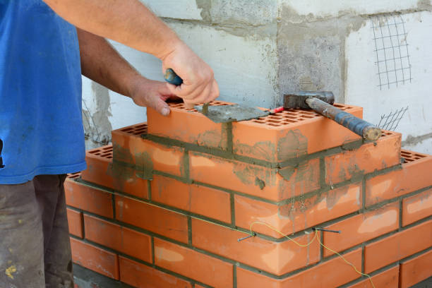 istock Masonry brickwork. A masonry contractor is laying the house corner with face bricks bonding them with a concrete block wall with a wire mesh using a trowel, mortar and a hammer. 1332628580