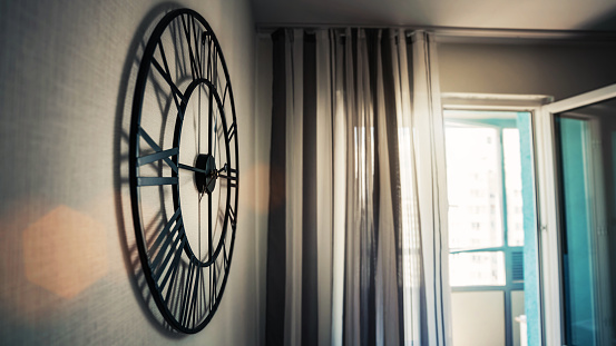 Big round black classical clock hangs on wall of kitchen room close side view low angle shot