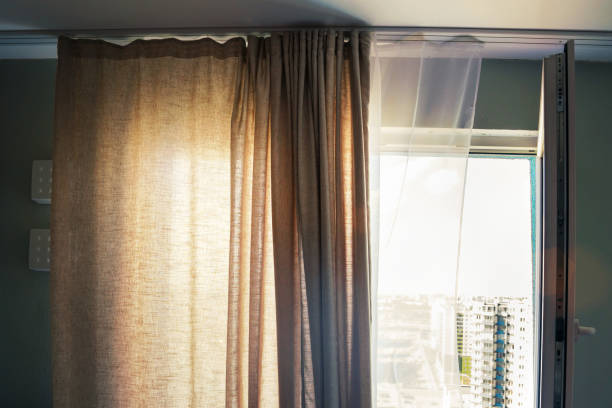 istock Dark beige dense curtain hangs on open window with bright sunlight 1332634925