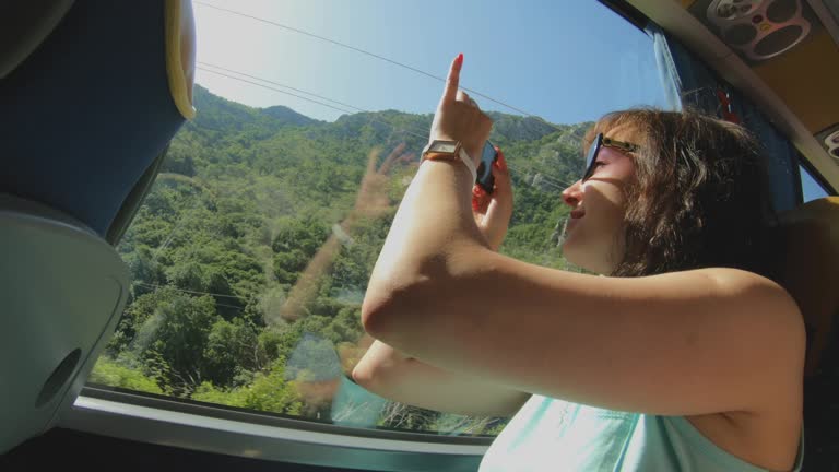 Tourist girl with smartphone takes pictures of nature landscape through bus window. Sightseeing trip and Travel. Vacation in Montenegro, excursion