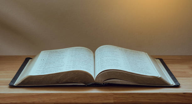 istock Open Bible on a wood table with light from window. 1332637561