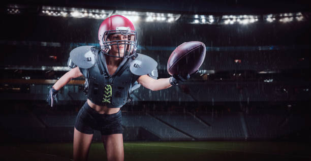 アメリカンフットボールチームの選手のユニフォームを着てスタジアムを横切ってボールを持って走っている女の子のイメージ。スポーツコンセプト。 - football player american football sports team teamwork ストックフォトと画像