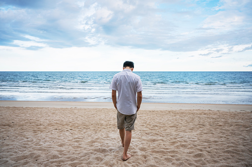 Rear of loneliness man in white shirt walking on the beach in the sea