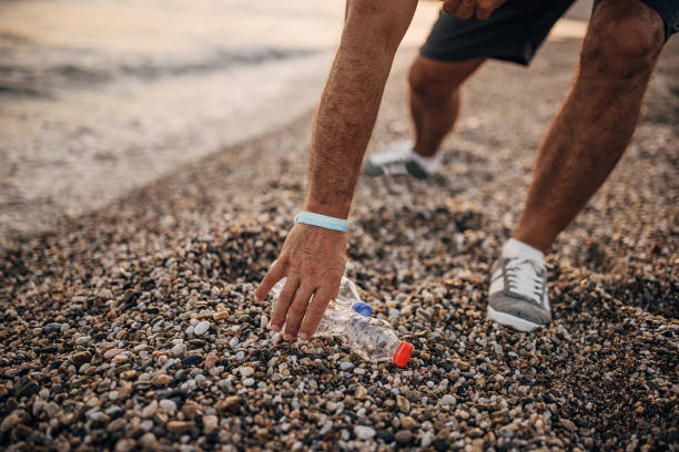 istock Man picking up plastic bottle on the beach 1332650167
