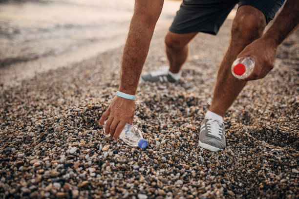 istock Man picking up plastic bottle on the beach 1332650199
