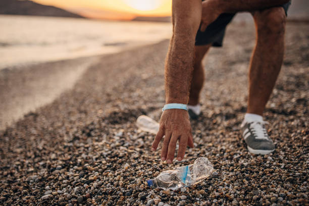 istock Man picking up plastic bottle on the beach 1332650236