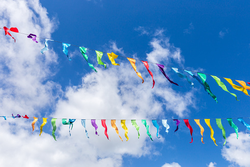 Colorful bunting flags in the wind. Festive background for holidays, anniversary, celebration. Multi-colored flag garland against a blue saturated sky