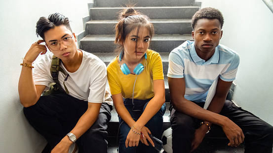 Portrait of multiracial group of teen high school students sitting on stairs looking at camera. Horizontal banner image. Back to school concept.