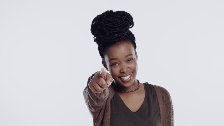 4k video footage of a young woman standing against a white background in the studio and pointing at the camera